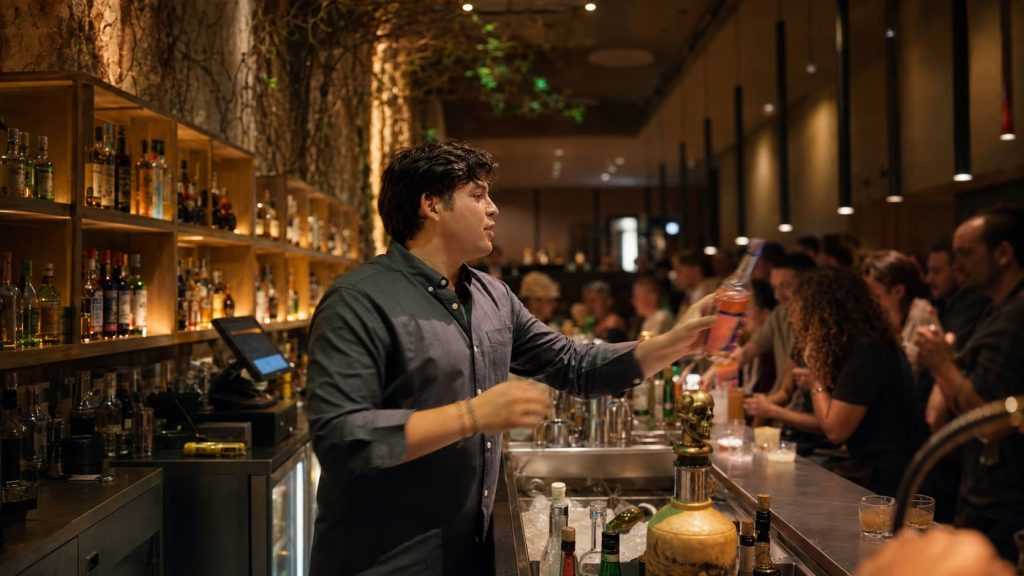 Bartender serving a cocktail at a busy bar